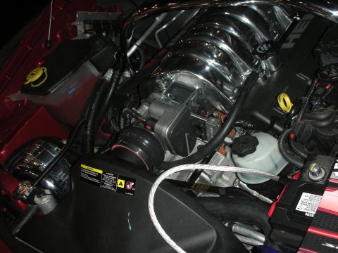 1998 Ford Crown Victoria - chrome intake manifold and supercharger pulley sit in the engine bay of a red car, with a yellow warning label visible.
