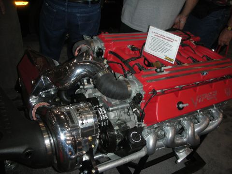 1998 Ford Crown Victoria - red-topped Viper V10 engine fitted with a polished centrifugal supercharger sits on a display stand with an info card.