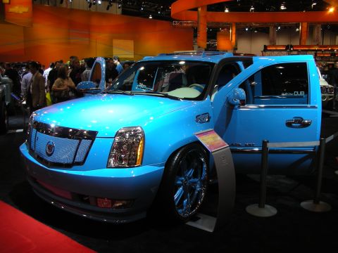 1998 Ford Crown Victoria - light-blue customized Cadillac Escalade with matching billet wheels and open doors is displayed at an auto show.