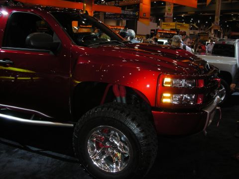 1998 Ford Crown Victoria - deep-red lifted Chevrolet Silverado on chrome wheels and mud tires shows its illuminated front end at a trade show.