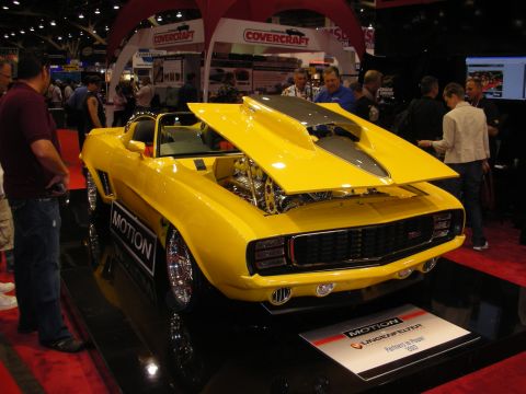 1998 Ford Crown Victoria - yellow custom Camaro by Motion sits with its hood up on a black stage in front of a Covercraft booth.