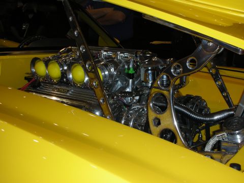 1998 Ford Crown Victoria - chrome engine fed by three yellow velocity stacks and surrounded by drilled brackets sits in a yellow custom car.