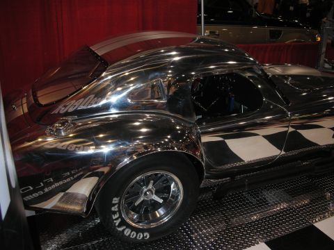 1998 Ford Crown Victoria - polished aluminum body of a Cobra-style roadster gleams in profile on chrome five-spoke wheels with Goodyear tires.