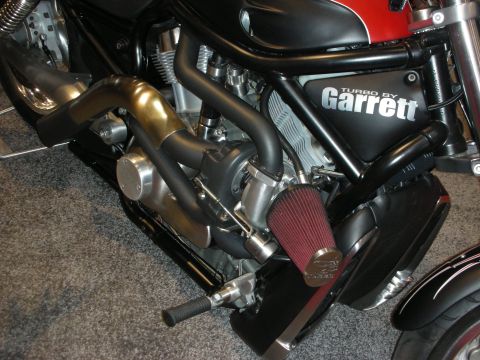 1998 Ford Crown Victoria - Close-up of a turbocharged motorcycle engine featuring a Garrett turbo, polished piping, and a red conical intake filter.