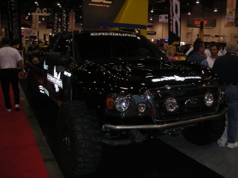 1998 Ford Crown Victoria - black lifted off-road pickup truck with a Ford front grille, fog lights, and bypass shocks on display at an indoor show.