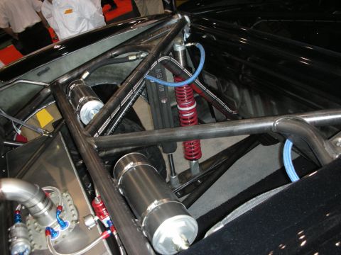 1998 Ford Crown Victoria - Close-up of a tube-frame chassis showing a red coilover shock, blue braided lines, and polished aluminum tanks.