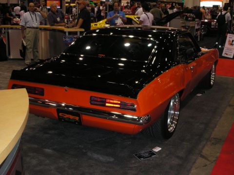 1998 Ford Crown Victoria - Rear three-quarter view of a black-and-orange first-generation Camaro with chrome wheels at an indoor show.