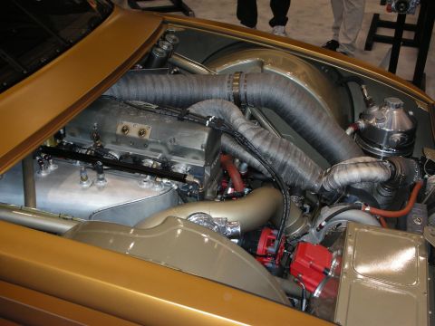 1998 Ford Crown Victoria - Engine bay of a gold-painted custom car showing flexible corrugated ducting, a polished compressor, and a red distributor.