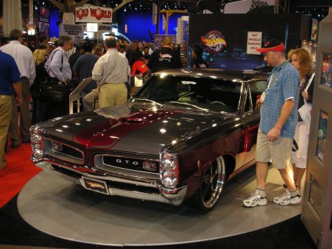 1998 Ford Crown Victoria - maroon-and-black restomod Pontiac GTO displayed on a turntable while spectators look on at an indoor show.