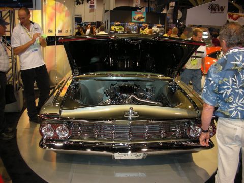 1998 Ford Crown Victoria - gold-and-black custom car with its hood open on a turntable, surrounded by spectators at an indoor show.