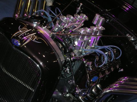 1998 Ford Crown Victoria - polished V8 engine with chrome individual-runner velocity stacks and blue plug wires in a dark pinstriped hot rod.