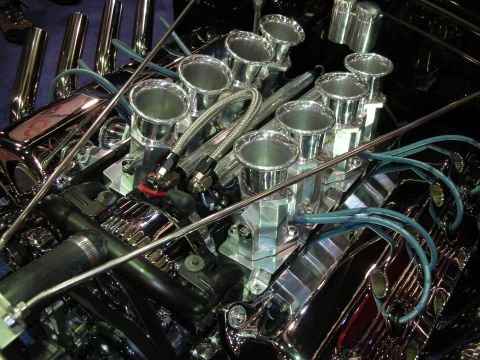 1998 Ford Crown Victoria - Detailed close-up of a chrome V8 engine's individual velocity stacks and teal spark plug wires.