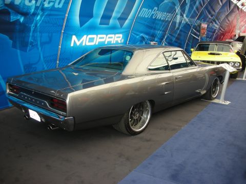 1998 Ford Crown Victoria - gray two-door muscle car shown rear three-quarter on a stand beside a blue Mopar backdrop, with a yellow car behind.