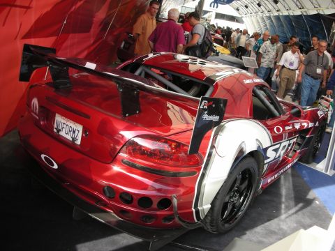 1998 Ford Crown Victoria - Rear three-quarter of a red chrome-wrapped Viper race car with a tall wing, parked indoors among onlookers.