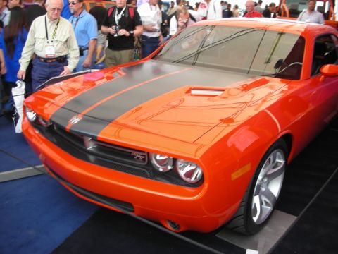 1998 Ford Crown Victoria - orange Dodge Challenger coupe with black hood stripes on a display platform amid a crowd at a car show.