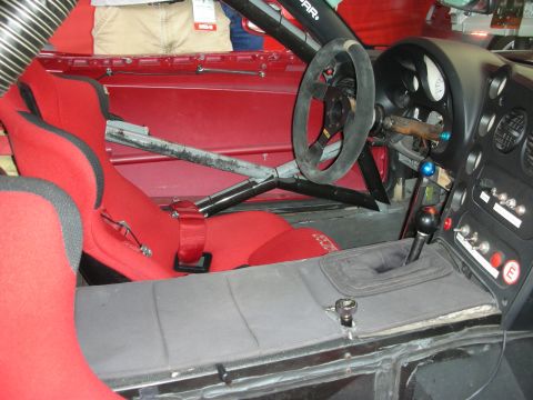 1998 Ford Crown Victoria - bare race car cockpit with a roll cage, red bucket seats, harnesses and a suede-rimmed steering wheel.