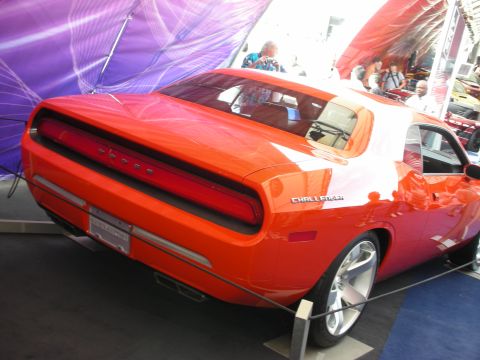 1998 Ford Crown Victoria - Rear three-quarter of an orange Dodge Challenger coupe with full-width taillight on a stand under a show tent.