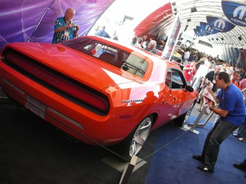 1998 Ford Crown Victoria - orange Dodge Challenger shown from the rear on a platform with a crowd and Mopar banners under a tent.