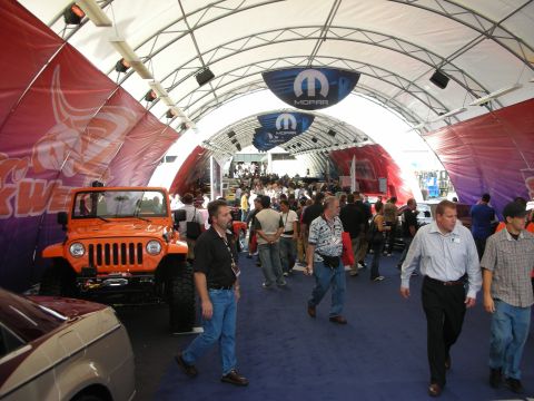 1998 Ford Crown Victoria - crowded indoor show tent with Mopar banners overhead and an orange lifted Jeep Wrangler at left.