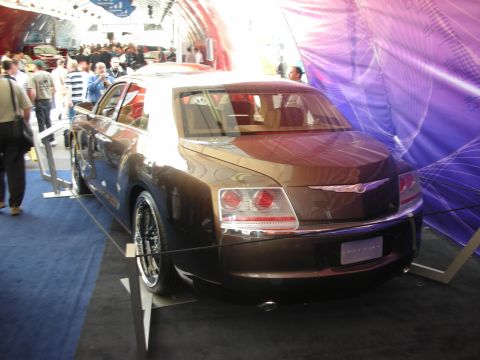 1998 Ford Crown Victoria - Rear three-quarter of a maroon Chrysler four-door sedan with round taillights on a stand under a show tent.