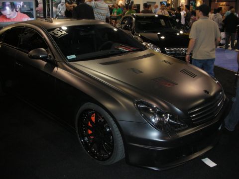 1998 Ford Crown Victoria - matte black Mercedes-Benz CLS four-door coupe with a vented hood and black wheels at an indoor show.