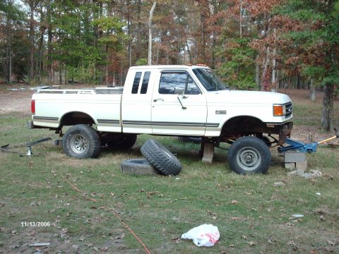 1990 Ford F-150 - White Ford F-250 pickup truck undergoing modifications, lifted on blocks with a jack supporting the front.