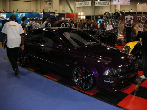 1998 Ford Crown Victoria - deep purple-black BMW sedan, lowered on black multi-spoke wheels, on a red-and-blue display floor at a show.