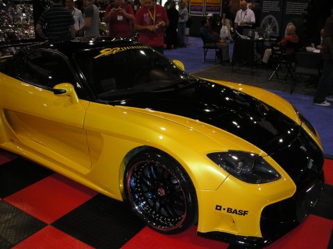 1998 Ford Crown Victoria - yellow sports coupe with a black hood and side stripe sits on a red-and-black checkered floor at an indoor show.
