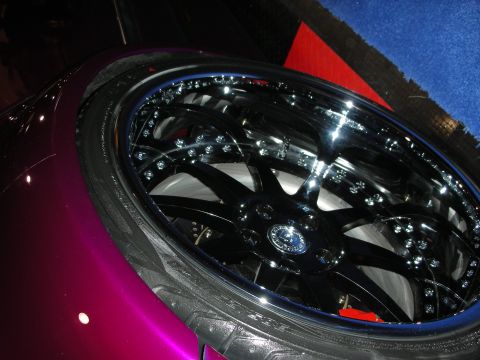 1998 Ford Crown Victoria - Close-up of a black multi-spoke wheel with chrome bolts on a magenta car parked over red and blue show carpet.