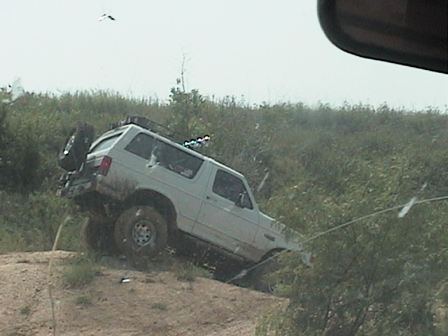 White Ford Bronco with roof lights climbing out of a rutted dirt bank off-road