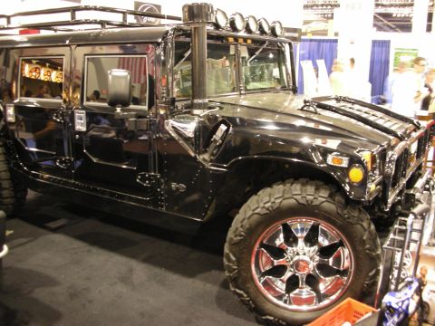 1998 Ford Crown Victoria - black Hummer H1 SUV with a roof rack, off-road light bar and chrome wheels on display at an indoor show.