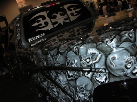 1998 Ford Crown Victoria - black show truck at an indoor event, its body airbrushed with grey skulls and rear window wearing tribal and BFGoodrich decals.
