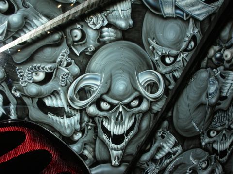 1998 Ford Crown Victoria - Close-up of an airbrushed ram-horned grey skull amid ghoulish faces painted on a vehicle's dark glossy body.