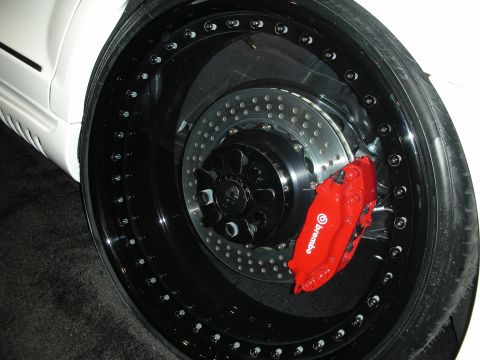 1998 Ford Crown Victoria - red Brembo brake caliper and cross-drilled rotor sit behind a black bead-lock alloy wheel on a white vehicle.
