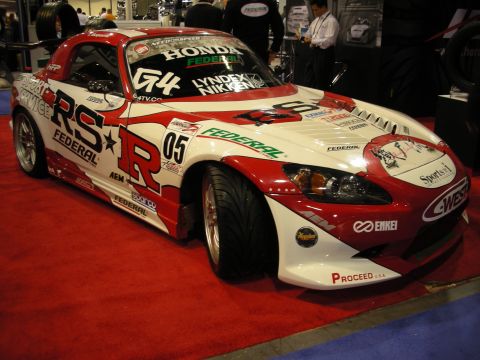 1998 Ford Crown Victoria - red-and-white Honda S2000 race car with RS-R and Federal livery sits on red carpet at an indoor show booth.