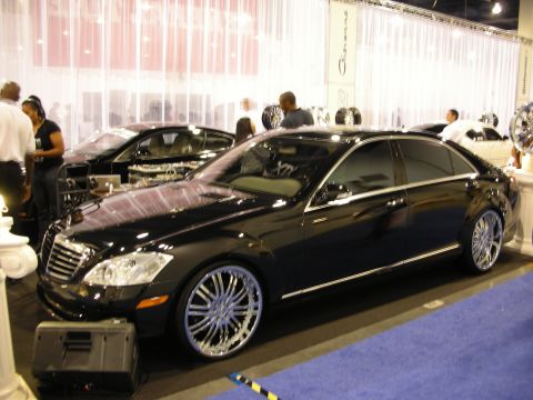 1998 Ford Crown Victoria - Side view of a black Mercedes-Benz S-Class on chrome multi-spoke wheels parked on blue carpet at an indoor show.