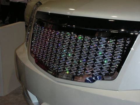 1998 Ford Crown Victoria - grille fully encrusted with multicolored crystals on the front of a cream-colored luxury SUV at an indoor display.