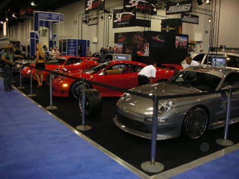 1998 Ford Crown Victoria - roped-off display of red Ferraris and a silver sports car on blue carpet at an indoor automotive show booth.