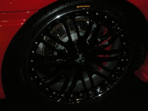 1998 Ford Crown Victoria - black multi-spoke bead-lock wheel on a Continental tire with a red brake caliper on a red sports car at a show.