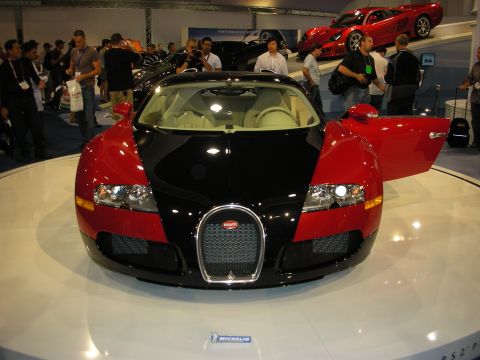 1998 Ford Crown Victoria - A two-tone Bugatti Veyron is displayed at an auto show with its door open, while other vehicles and attendees are visible.