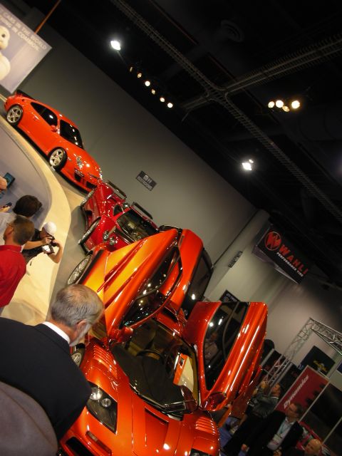 1998 Ford Crown Victoria - Multiple exotic cars are showcased at an automotive event, including a vibrant orange sports car with distinctive butterfly doors.