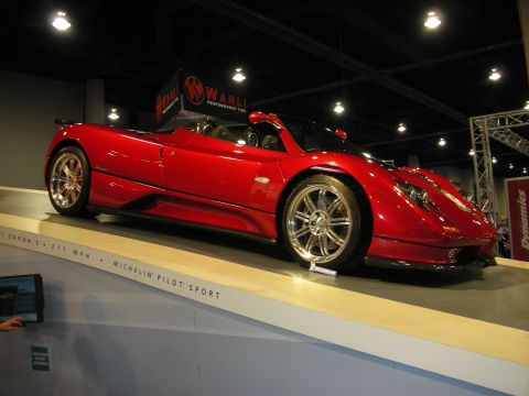 1998 Ford Crown Victoria - A red convertible sports car is displayed on a ramp at an indoor event, with 'Michelin Pilot Sport' text visible.