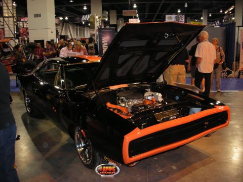 1998 Ford Crown Victoria - black second-gen Dodge Charger with its hood up reveals a chrome engine and orange-accented bay surrounded by show crowds.
