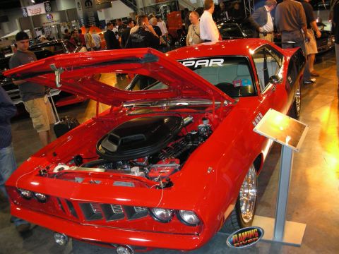 1998 Ford Crown Victoria - bright red Mopar muscle coupe with raised hood and visible engine sits on display under show lighting with onlookers.