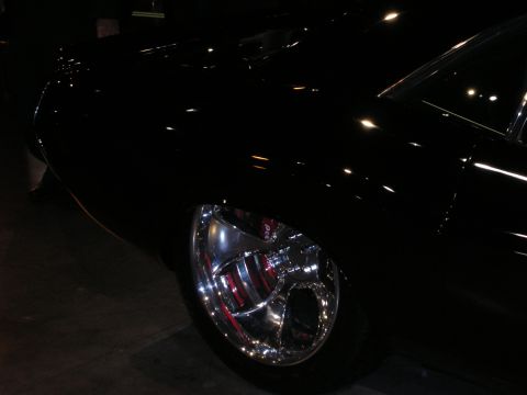 1998 Ford Crown Victoria - polished five-spoke wheel reflects light on a glossy black show car parked in a dimly lit hall.