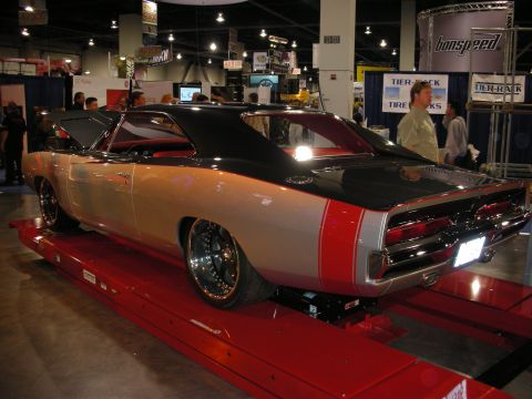 1998 Ford Crown Victoria - custom Dodge Charger in tan and red with a black roof and rear spoiler sits on a red display ramp at an indoor show.