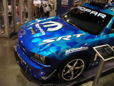 1998 Ford Crown Victoria - blue camo-wrapped Dodge Charger SRT with Mopar and BFGoodrich graphics on a display ramp at an indoor show.