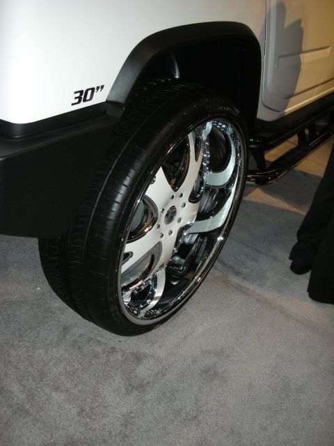 1998 Ford Crown Victoria - massive 30-inch chrome multi-spoke wheel with a thin low-profile tire mounted on a white SUV at an indoor show.