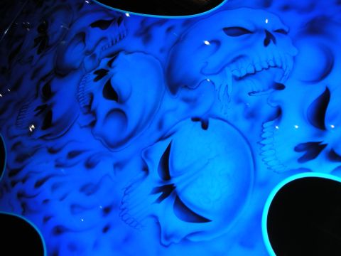 1998 Ford Crown Victoria - Glowing blue airbrushed skulls and flames painted on a glossy black vehicle body panel under show lighting.
