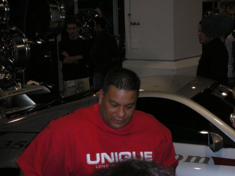 1998 Ford Crown Victoria - man in a red 'UNIQUE Long Island' T-shirt looks down beside a white show car with display wheels behind him.